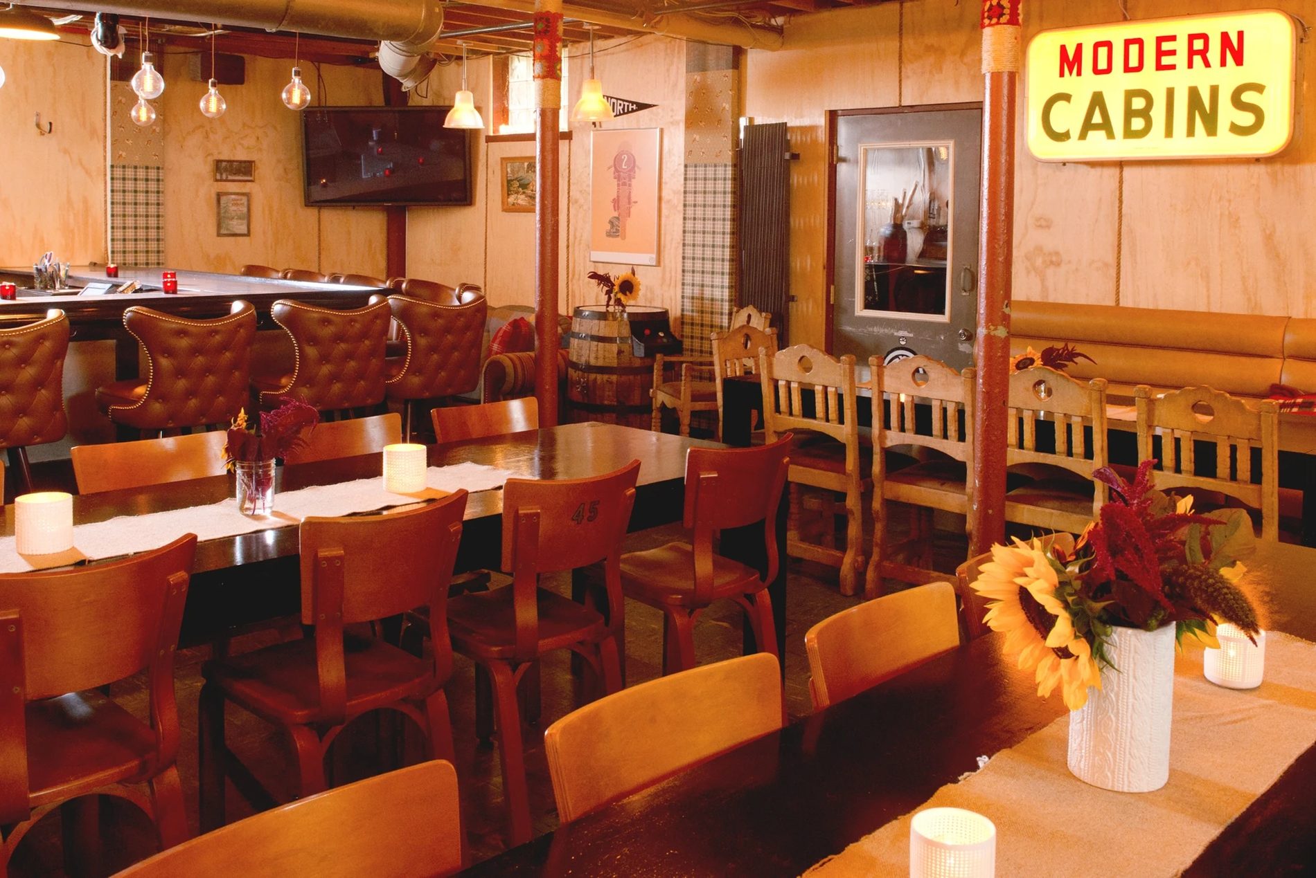 A long private dining room with wooden tables, booths and the Modern Cabins neon sign