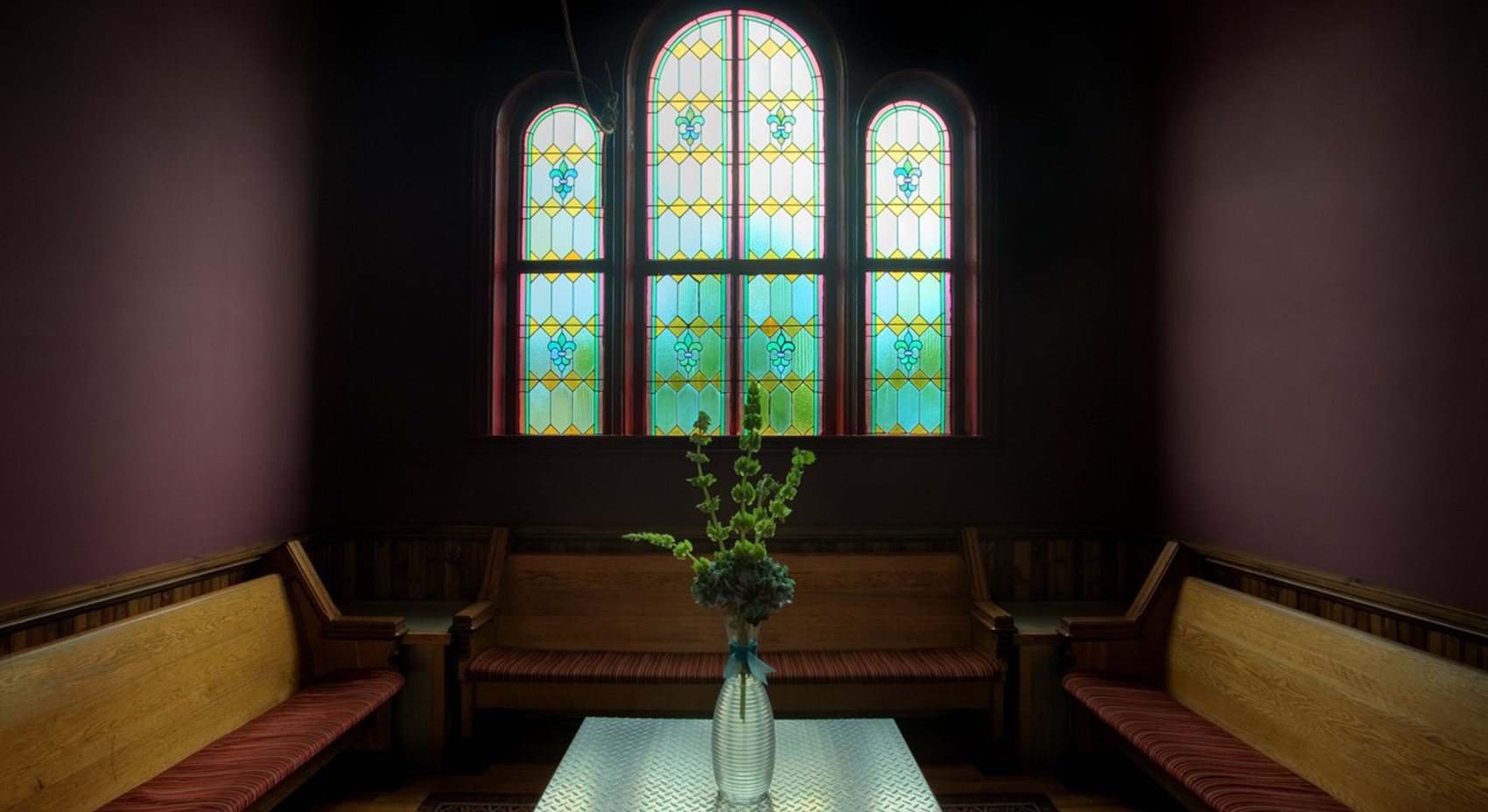 A church pew booth beneath a restored stained glass window